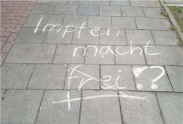 "Impfen macht frei" steht mit Kreide geschrieben auf einem Gehweg.