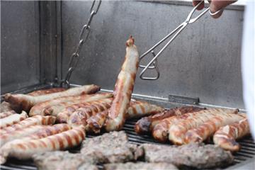 Bratwürste und anderes Fleisch liegen auf einem Holzkohlegrill. 