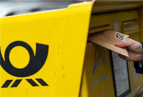 Eine Hand steckt einen Brief in einen Briefkasten.