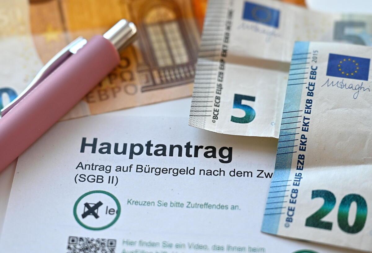 Der Hauptantrag für Bürgergeld liegt neben Geldscheinen auf einem Tisch. 