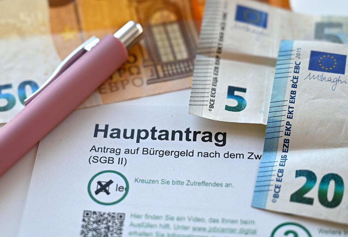 Der Hauptantrag für Bürgergeld liegt neben Geldscheinen auf einem Tisch. 