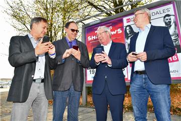 Schritt zu freiem WLAN: Bürgermeister Paul Bödeker (Zweiter von rechts) und seine Mitarbeiter haben schon einmal die Handys gezückt. Noch gibt es an der Werbetafel kein freies WLAN. Aber mit den neuen Verträge hat sich die Stadt das Recht gesichert, die Tafeln als Hotspots zu nutzen.