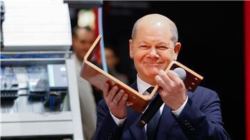 Bundeskanzler Olaf Scholz (SPD) hält eine Stromschiene für Energieverteilung am Stand von Rittal.