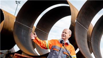 Bundeskanzler Olaf Scholz (SPD) steht vor Bauteilen für die Stahlfundamente von Windkraftanlagen.