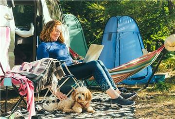 Eine Frau sitzt mit ihrem Hund auf einem Campingplatz. Camping erfreut sich immer größerer Beliebtheit. Doch Camping mit Hund stellt besondere Anforderungen. Hier gibt es die Top 5 hundefreundlichsten Campingplätze in Deutschland 2025.