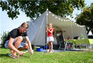 Ein Mann und ein Mädchen bauen ein Campingzelt auf. Haftpflicht und Hausrat: Wer die richtigen Versicherungen abschließt, kann sich beim Camping einiges an Stress sparen. 