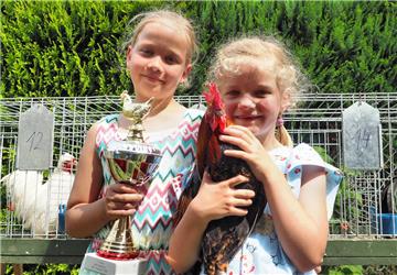Carita (7) hält Hahn Justus in Händen, den Sieger des Hähnekrähwettbewerbs
beim Bauernmarkt. Schwester Tjede (9) hält den Siegerpokal. 