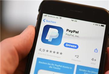 Die Applikation von PayPal ist auf einem Mobilfunkgerät zu sehen, das ein Mann in der Hand hält.
