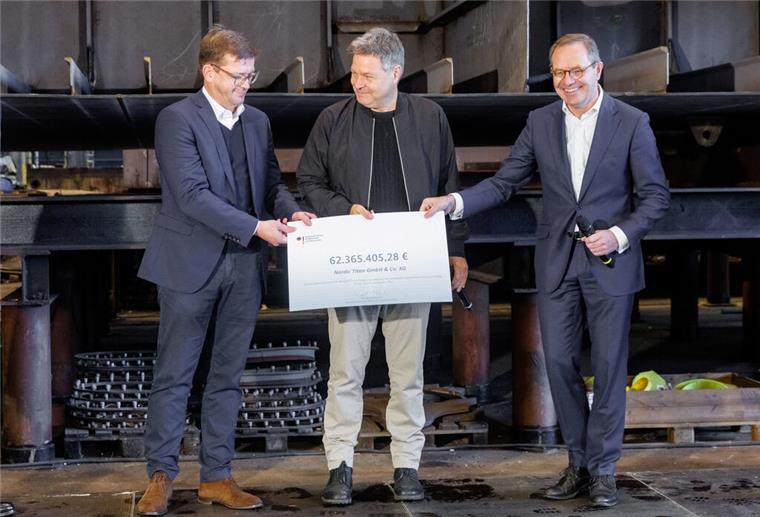 Habeck übergibt Förderbescheide für Bau von drei LNG-Schiffen Drei Männer stehen vor einem Schiffsbauteil und halten einen symbolischen Scheck in den Händen