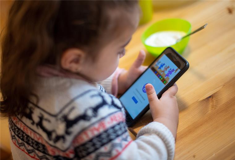 Tipps für Eltern, wenn Kinder sich das erste Handy wünschen Ein Mädchen spielt mit einem Smartphone in einer Unterkunft für geflüchtete Frauen.