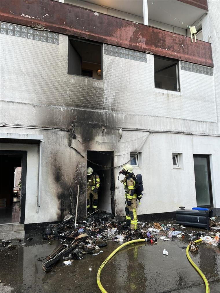 Mülltonnen in Flammen: Feuerwehr muss bei Brand in Lehe schnell eingreifen Zwei Feuerwehrleute stehen bei einem Haus, Ruß ist an der weißen Häuserwand zu sehen. Es handelt sich um einen Brand mehrerer Mülltonnen. Dank des schnellen Eingreifens der Feuerwehr konnte ein Übergreifen der Flammen auf das Wohngebäude in Lehe verhindert werden.