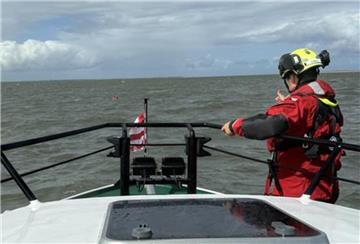 Ein Mann schwimmt mit Rettungsweste in der Nordsee. Ein Bott der Seenotretter nähert sich an, um den Schiffsbrüchigen zu retten.