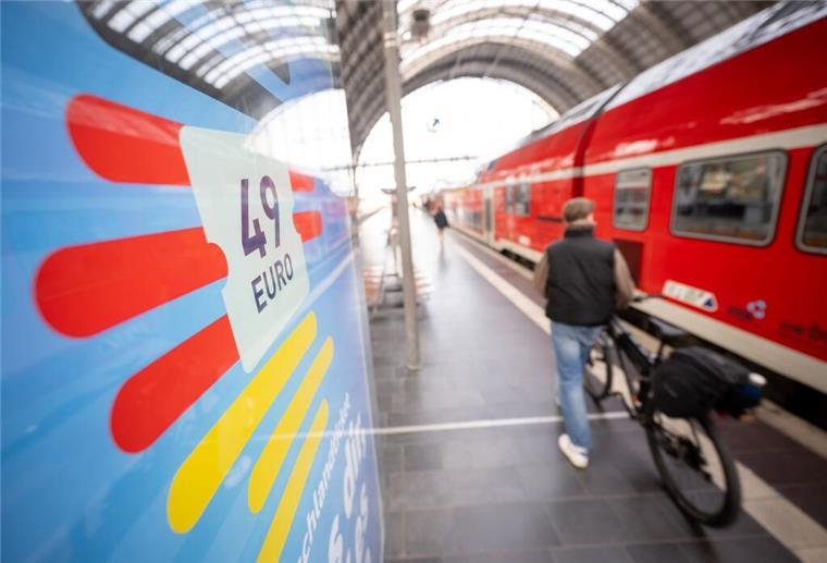 Deutschlandticket wird teurer - doch ihr müsst vorher zustimmen Ein Mann geht am Frankfurter Hauptbahnhof mit seinem Fahrrad zwischen der Werbung für das Deutschlandticket und einer Regionalbahn entlang.
