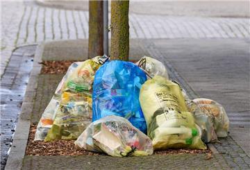 Müll in gelben Säcken liegen am Straßenrand, mittendrin liegt ein blauer Müllsack. 