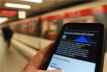 Ein Fahrgast hält ein Smartphone mit einem digitalen Deutschlandticket an einer U-Bahnstation in der Hand.