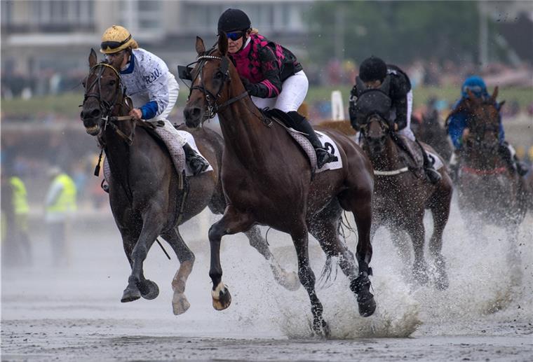 Galopper reiten am 16.07.2017 über das Watt vor dem Strand von Duhnen in Cuxhaven (Niedersachsen) und lassen das Meerwasser hochspritzen