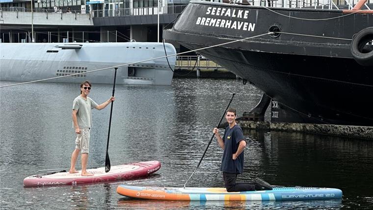 Wassersport und Kultur: So soll der Alte Hafen zur Sail zur Erlebniswelt werden Zwei Männer demonstrieren Stand-up-Paddling in einem Hafen. Im Hintergrund sind ein U-Boot und ein Schiff zu sehen.