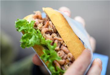 Eine Frau hält ein Krabbenbrötchen in der Hand.