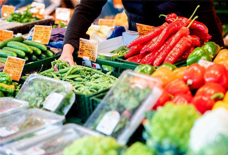Das Leben in Deutschland ist extrem teuer geworden Ein Verkäufer greift an einem Obst- und Gemüsestand auf dem Wochenmarkt in eine Kiste mit Erbsen.