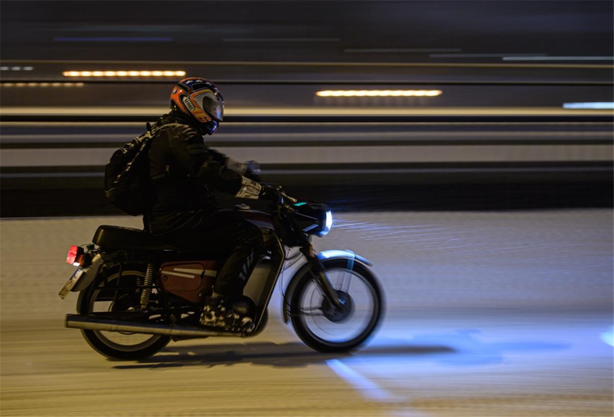 Ein Mann fährt mit einem Moped bei Schneefall über eine verschneite Straße in der Innenstadt. 