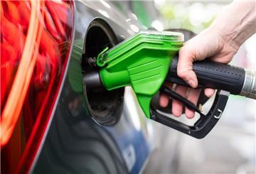  Eine Frau hält an einer Tankstelle an einer Zapfsäule eine Zapfpistole in der Hand und betankt ein Auto. 