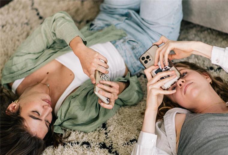 Zwei junge Frauen liegen auf dem Rücken und schauen in ihre Handys.
