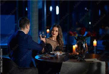 Junges Paar sitzt in einem edlen Restaurant und stößt mit einem Glas Wein an.