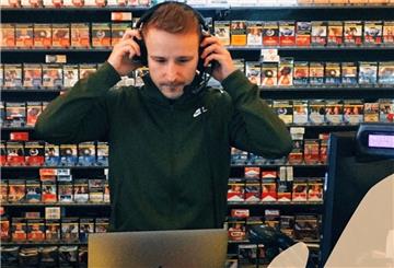 Mann mit Kopfhörern steht in Kiosk vor Zigarrettenregal