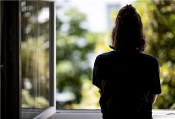 Eine Frau steht in ihrer Wohnung an einem Fenster.