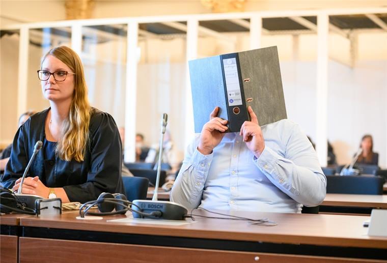 Prostituierte erwürgt - Neun Jahre Haft für 32-Jährigen Ein Mann hält in einem Gerichtssaal einen Aktenordner vor das Gesicht. Daneben sitzt eine Frau.