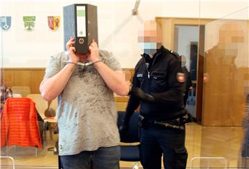 Der Angeklagte wird in Handschellen an seinen Platz im Schwurgerichtssaal des Landgerichts Stade gebracht. Vor sein Gesicht hält er einen Aktenordner.