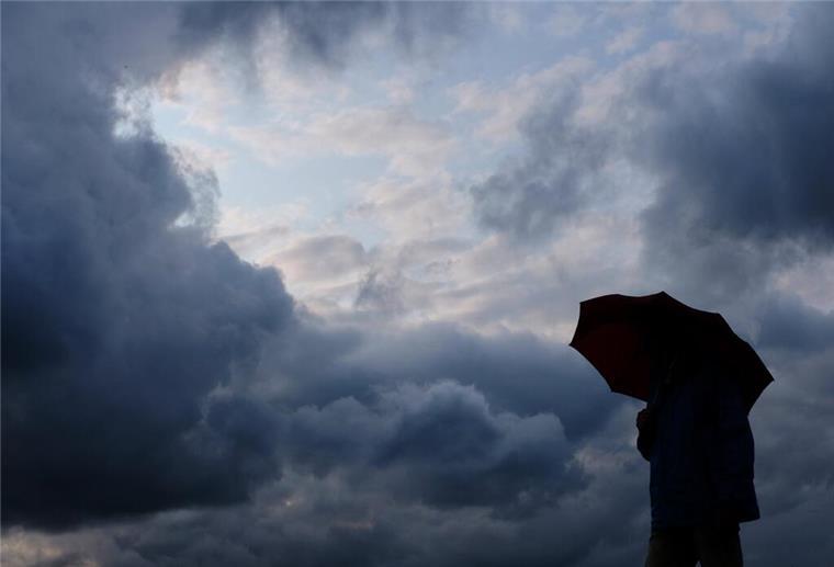 Starke Böen und vereinzelt Gewitter: So wird das Wetter im Norden Ein Mann geht bei stark bewölktem Himmel mit einem Regenschirm spazieren.