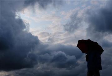  Ein Mann geht bei stark bewölktem Himmel mit einem Regenschirm spazieren. 