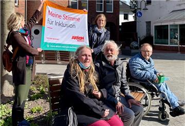 Der Banner wird von den Organisatoren der Aktion, Xenia Wakengut (links) und Anne Blankemeyer vom Fachdienst Teilhabe des Sozialwerks Wesermarsch, gehalten. Auf der Bank sitzt die Bewohnervertretung der Sozialstation Wesermarsch (vorne links): Beate Bartels, Peter Heuer und Frank Becke.