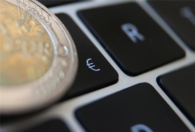 Eine Zwei-Euro-Münze liegt auf der Tastatur eines Laptops neben einem Eurozeichen. 
