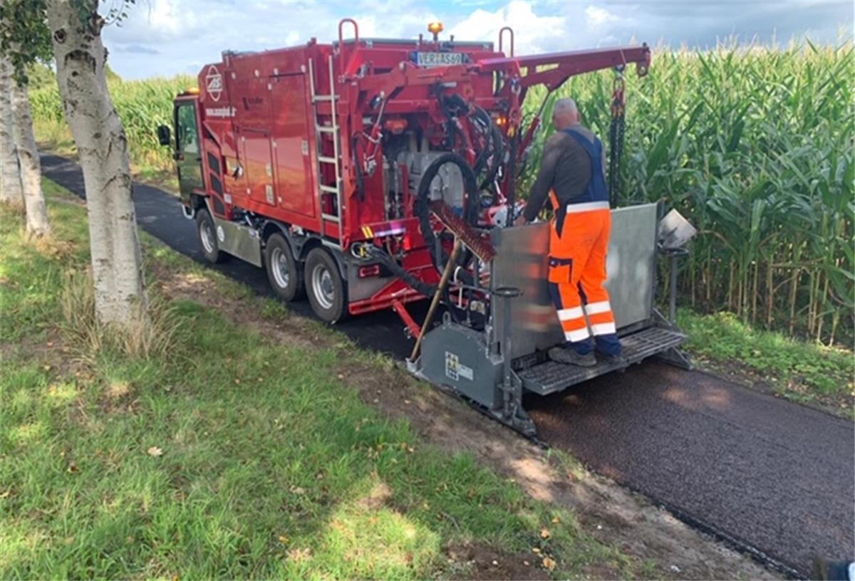 Der Fertiger im Einsatz: Entlang der Straße Hollenerheide in Hollen wurde hat ein Radweg mit einer neuer Methode eine neue Asphaltdecke erhalten.