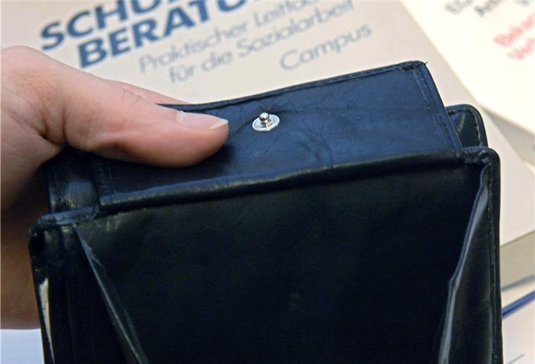 Ein fast leerer Geldbeutel wird bei der Schuldnerberatung der Caritas in Hannover über Bücher zur Schuldnerberatung und der Insolvenzordnung gehalten