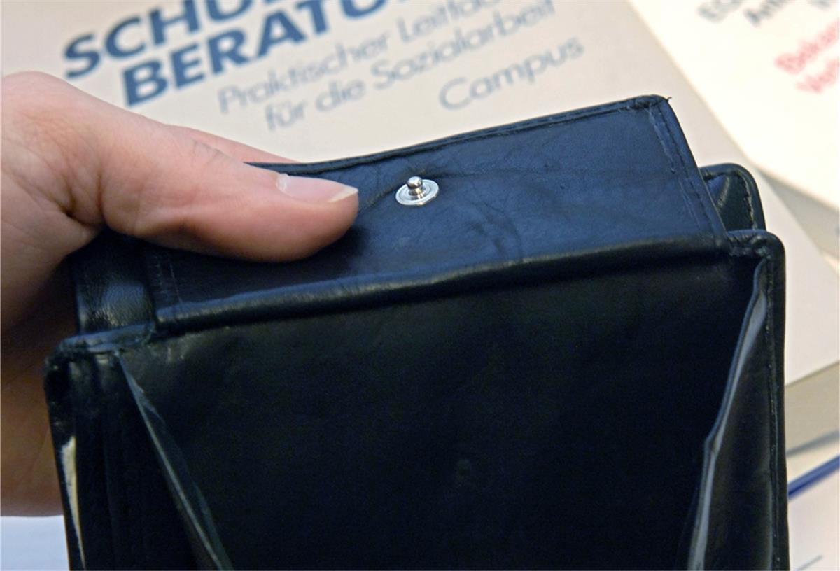 Ein fast leerer Geldbeutel wird bei der Schuldnerberatung der Caritas in Hannover über Bücher zur Schuldnerberatung und der Insolvenzordnung gehalten
