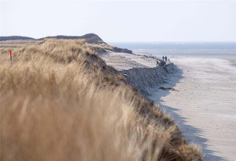Spaziergänger laufen an der Abbruchkante am Strand entlang. 