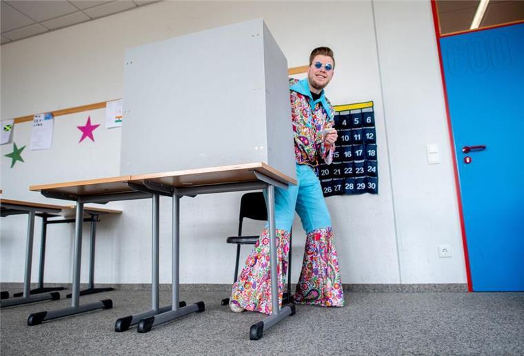 Dinosaurier, Elvis und Co. stürmen das Wahllokal! Der kostümierte Wähler Nico verlässt in einem Wahllokal nach der Stimmabgabe den Sichtschutz der Wahlkabine.