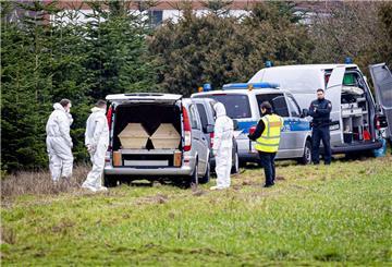 Mitarbeiter der Spurensicherung der Polizei stehen an einem Leichenwagen, der auf einer Wiese parkt. 