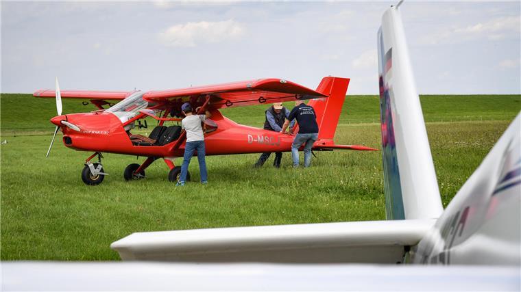Ein rotes Flugzeug und drei Menschen auf einem Feld.