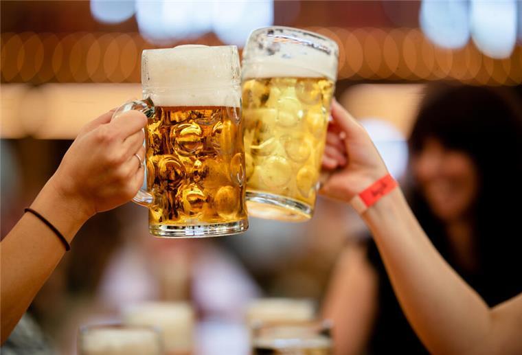 Macht Schnaps wirklich schneller betrunken als Bier? Alkohol-Mythos entlarvt! Menschen in einem Festzelt stoßen mit Bier an.