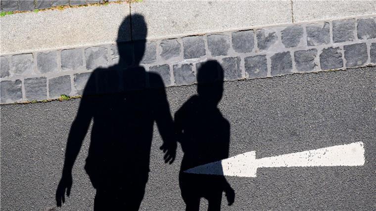 Mehr Alleinerziehende in Armut Der Schatten von einem Mann und einem Kind sind auf einer Straße mit einem Pfeil zu sehen.