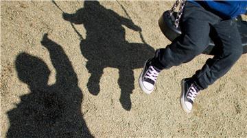 Der Schatten von einem Mann und einem schaukelnden Kind auf einem Spielplatz.
