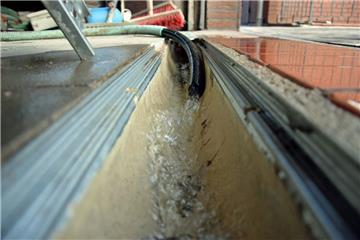 Der Schlauch liegt in der Ablaufrinne. 10 Liter Wasser sprudeln innerhalb von 10 Sekunden heraus. Tagtäglich fördert die Pumpe aus dem Pumpensumpf mehr als 86 000 Liter Wasser. Trotz neuer Drainage drückt das Grundwasser in den Keller. des Wulsdorfer Hauses.