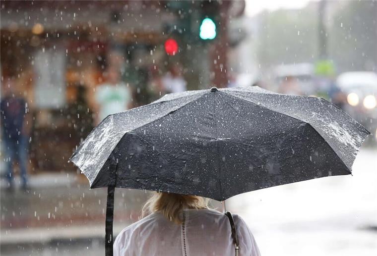 Auch am Wochenende gibts in Niedersachsen und Bremen Schauer - und Gewitter Ein Frau steht bei einem kurzen Regenschauer mit einem Regenschirm an einer Ampel
