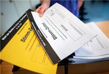 Ein Wahlhelfer gibt in einem Wahllokal die Stimmzettel für die Bürgerschaftswahl und die Kommunalwahl an die Wähler aus. 