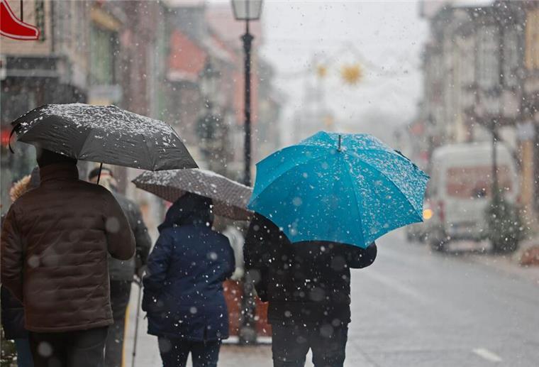 Menschen gehen mit Regenschirm bei Schneeregen am Montagvormittag durch die Innenstadt von Wernigerode.