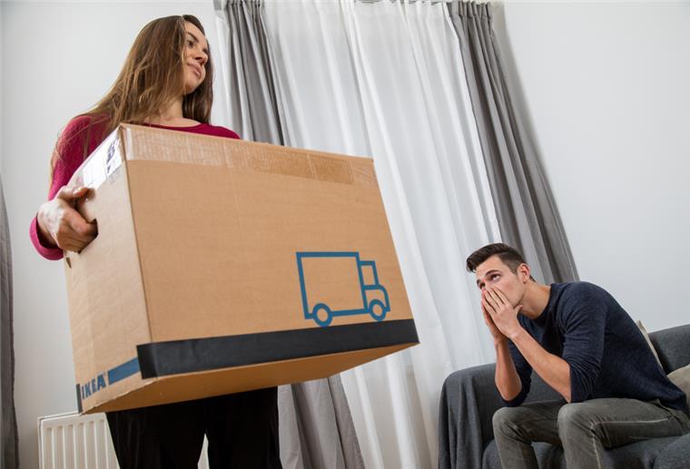 Zahl der Scheidungen fällt 2021 in Niedersachsen auf Tiefstand Eine Frau packt ihre Sachen während ihr Mann auf dem Sofa sitzt.